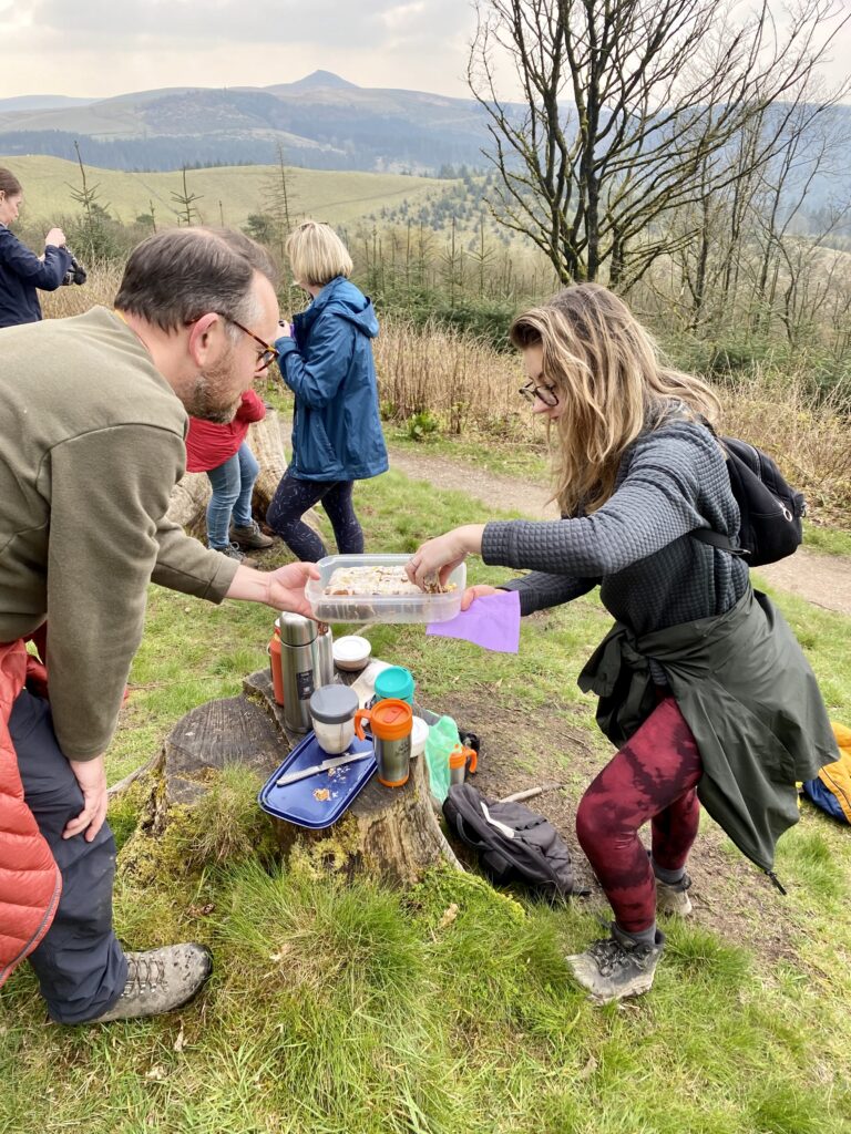 man offering woman a slice of cake in the countryside.